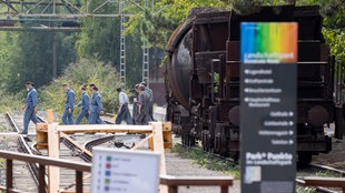 Statisten gehen 2022 im Rahmen der Dreharbeiten zum Film "Die Tribute von Panem: Das Lied von Vogel und Schlange" im öffentlichen Teil des Landschaftsparks am Erkennungszeichen des Parks vorbei, einer alten Lok