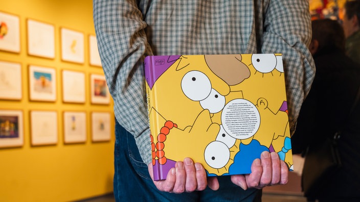 Ein Mann hält hinter seinem Rücken ein Buch über die Simpsons in der Ausstellung "Die Simpsons: Gelber wird's nicht" in Dortmund.