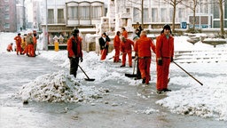 1979. Straßenreiniger kehren die Schneemassen in der Kölner Innenstadt zusammen.