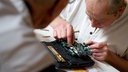 Ein ehrenamtlicher Helfer unterstützt im Repair Cafe in Berlin-Spandau einen Rentner bei der Reparatur eines defekten DVD-Players.