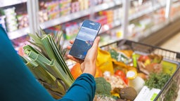 Frau mit Smartphone und Einkaufswagen im Supermarkt