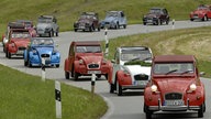 13 Enten (Citroën 2CV) fahren auf einer Straße