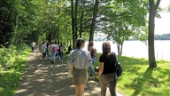 Menschengruppe spaziert am Baldeneysee entlang. 