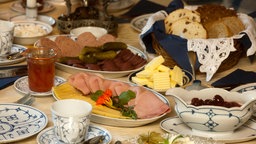 Eine üppig gedeckte Bergische Kaffeetafel mit Rosinenstuten, Wurst, Schinken, Käse, Birnenkraut, Apfelkraut, Quark, Butter und Kirschen.