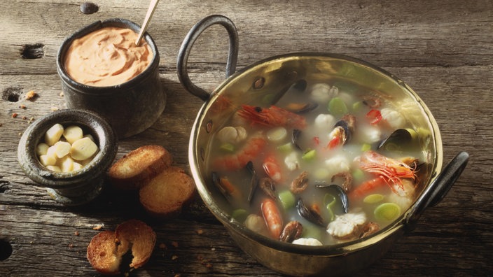 Bouillabaisse, die traditionelle französische Fischsuppe in einer eisernen Schale auf hölzernem Tisch.