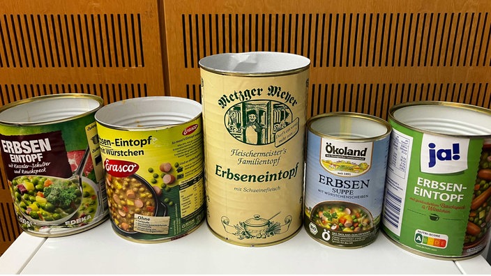 Fünf Dosen Erbseneintopf und Erbsensuppe verschiedener Anbieter stehen im WDR-5-Studio nebeneinander.