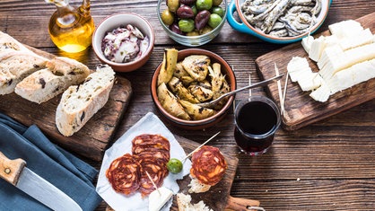 Typische Auswahl an spanischen Tapas, u.a. Salami, Oliven und Sardellen, auf einem Tisch. 