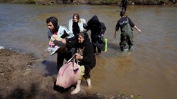 Syrische Familien flüchten nach einem Massaker an Alawiten im März 2025 über einen Grenzfluss in den Libanon