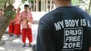 Buddhistisches Drogenentzugskloster Wat Thamkrabok in Thailand: Auf dem Rücken des T-Shirts eines Studenten steht die Aufschrift "my body is a drugfree zone",; im Hintergrund in roten Gewändern sind Mönche des Klosters zu sehen.