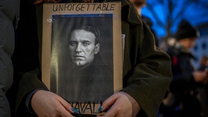 Eine Demonstrantin hält am 16.02.2024 vor der russischen Botschaft in Berlin ein Schild mit einem Porträt von Alexej Nawalny vor ihrer Brust. Darauf steht "Unforgettable Nawalny" geschrieben.