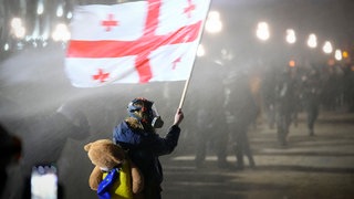 Demonstrant hält georgische Nationalflagge, während er vor dem Parlament mit einem Wasserwerfer besprüht wird, 03.12.2024. 