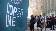 Besucher füllen Wasserflaschen neben einer Fahne mit der Aufschrift "COP28 UAE"