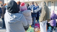 Geflüchtete aus der Ukraine stehen mit Rücksäcken und Taschen vor den Gebäuden einer Flüchtlingsunterkunft in Köln