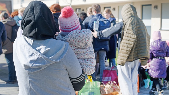 Geflüchtete aus der Ukraine stehen mit Rücksäcken und Taschen vor den Gebäuden einer Flüchtlingsunterkunft in Köln