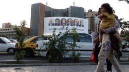 Eine Familie läuft auf einer Straße in Teheran, Ira vor einem Poster, das die Kandidaten der Präsidentschaftswahl zeigt