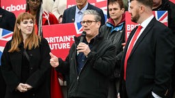 Labour-Chef Keith Starmer steht zwischen Labourfunktionären und Anhängern mit Plakaten und spricht in ein Mikrofon