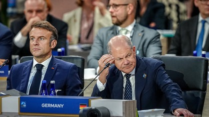 Frankreichs Präsident Emmanuel Macron und Bundeskanzler Olaf Scholz sitzen beim Nato-Gipfel nebeneinander.