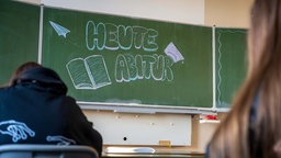 Symbolbild: Rückansicht von Schüler:innen vor einer Tafel, auf der "Heute Abitur" steht.