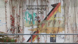 Auf einer abgeblätterten Mauer ist der Aufdruck "Gemeinschaftswerk Aufschwung Ost" mit Graffitis übersprüht.