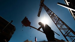 Symbolbild: Ein Mensch schaufelt im Gegenlicht Erde auf einer Baustelle.