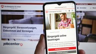 Bildschirm und Smartphone-Display mit Informationen des Jobcenters zum Bürgergeld.