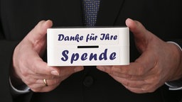 Mann hält eine Kiste mit der Aufschrift: Danke für Ihre Spende, Symbolbild