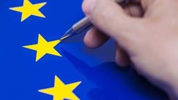 Symbolfoto: Hand mit Kugelschreiber über der EU-Fahne