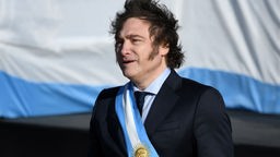 Javier Milei mit einer Schärpe in Argentiniens Landesfarben blau und weiß vor einer argentinischen Flagge