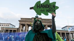 Grün verkleidete Aktivistin der Gruppe "Extinction Rebellion" hält ein Plakat in FOrm eines Eichenblattes auf dem steht "Handeln statt hoffen"