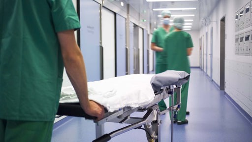 Symbolbild: Medizinisches Personal mit OP-Liege in einem Krankenhausflur.