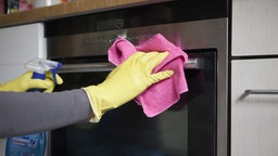 Eine Frau putzt mit einem Lappen und Reinigungsmittel den Backofen. Symbolbild Frühjahrsputz