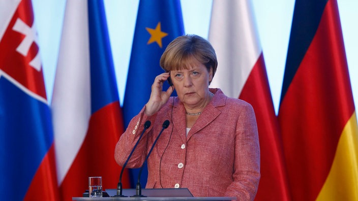 Merkel mit konzentriertem Blick auf Redetribüne vor Flaggen u.a. Polen, Deutschland, EU