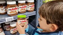 Ein kleiner Junge hält im Supermarkt ein Glas Nutella in veganer Version in der Hand. 