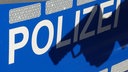 Schatten einer Waffe auf dem Schriftzug "POLIZEI" an der Tür eines Einsatzfahrzeugs. Symbolbild