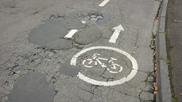Ein Radweg-Symbol auf einer maroden Straße voller Flicken