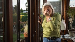 Eine Rentnerin stützt sich mit Schwindelgefühlen an einem Fensterrahmen ab. 