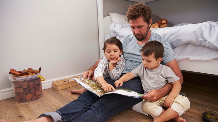 Ein erwachsener Mensch liest zwei Kindern vor.