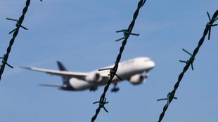 Ein Flugzeug der Fluggesellschaft Lufthansa, im Landeanflug auf den Flughafen Frankfurt a.M. Im Vordergrund Stacheldraht. Symbolbild zum Thema Abschiebeflug. 