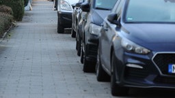 In einer Straße sind Autos zur Hälfte auf dem Gehweg geparkt. 