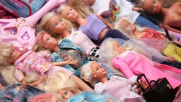 Mehrere klassische Barbie-Puppen in verschiedenen Puppenkleidern liegen auf einer Fläche.