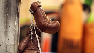 Braunfarbene Boxhandschuhe hängen an einer Wand.