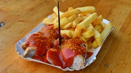 Eine Currywurst mit Pommes serviert in einer Schale.