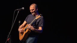 Danko Rabrenović performt mit Gitarre und Mikrofon auf einer Bühne.