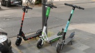 Drei E-Scooter stehen an einer Straße.