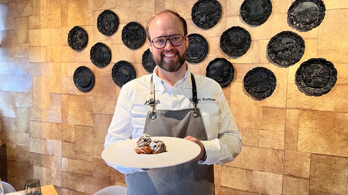 Sternekoch Jürgen Kettner mit einem Teller Nougatknödel in der Hand. 