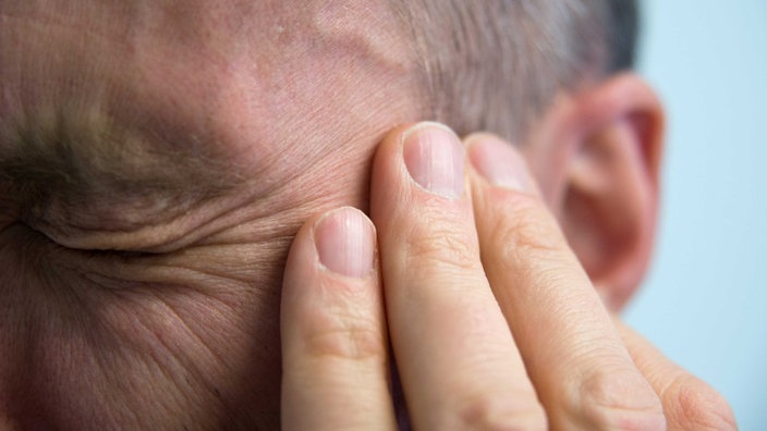 Ein Mann schließt die Augen und fasst sich an den Kopf