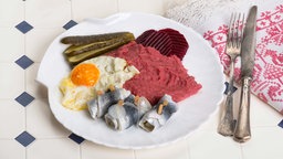 Labskaus mit Spiegelei, Rollmops, Gewürzgurken und Roter Beete auf einem Teller