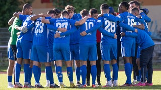 Spieler von Makkabi Berlin stehen vor dem Anpfiff auf dem Spielfeld und tragen Armbinden aus schwarzem Stoff. 