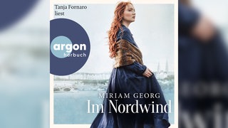 Das Cover von Miriam Georgs Roman "Im Nordwind" zeigt eine stolze, rothaarige Frau in blauem Kleid vor einer Küsten-Kulisse.