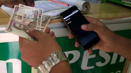 Ein Kunde tätigt eine mobile Geldüberweisung, bekannt als M-Pesa, an einem Safaricom-Vertreterstand, während er kenianische Schillinge in Nairobi, Kenia, hält.